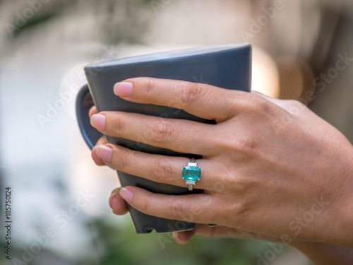 Closeup female hand holding coffee cup and wearing green gem ring photo