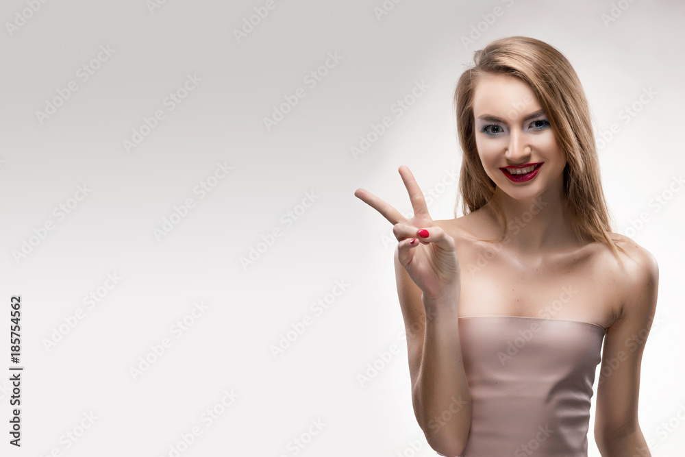 The beautiful blonde red lips smiling girl shows the sign victory. The beautiful blonde red lips smiling girl shows the sign victory.