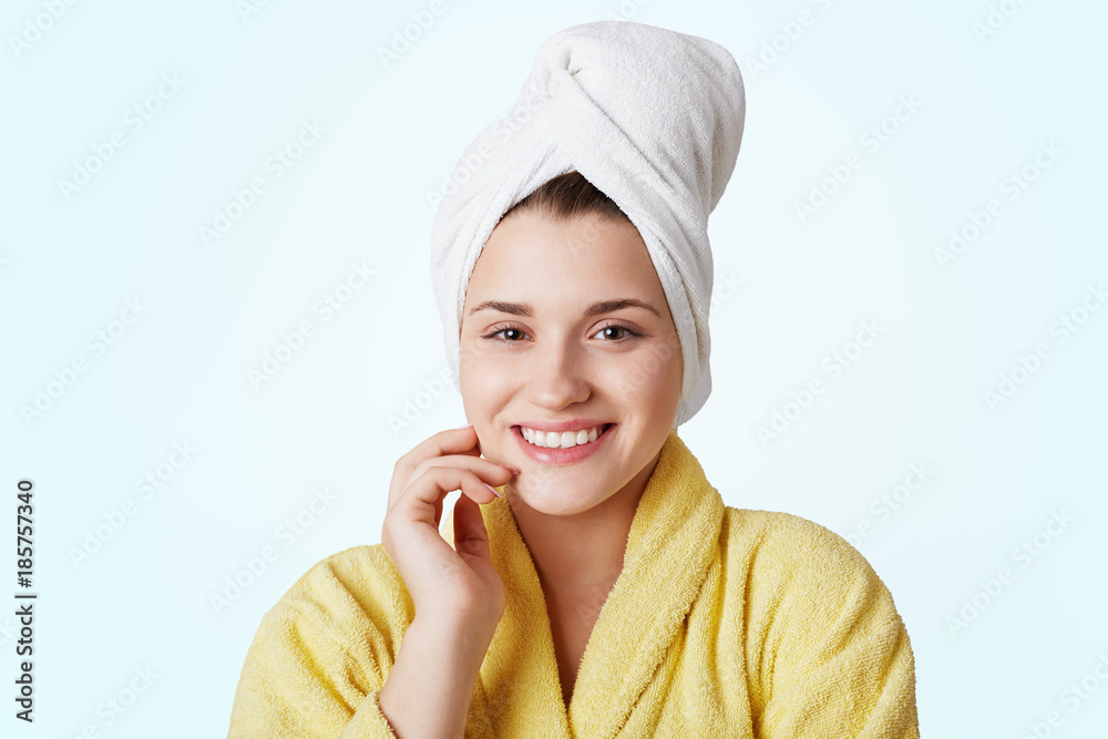 Body care and spa concept. Pretty beautiful young woman wears yellow bathrobe and towel on head, has pleasant smile, being content after taking shower or bath, isolated over white background. Body care and spa concept. Pretty beautiful young woman wears yellow bathrobe and towel on head, has pleasant smile, being content after taking shower or bath, isolated over white background.