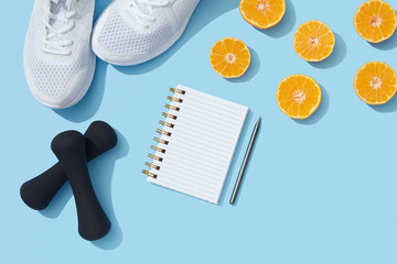 Female fitness flat lay, sneakers, dumbbells, notebook planner on blue background, healthy sports lifestyle New Year resolution