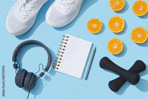 Female fitness flat lay, sneakers, dumbbells, notebook planner on blue background, healthy sports lifestyle New Year resolution