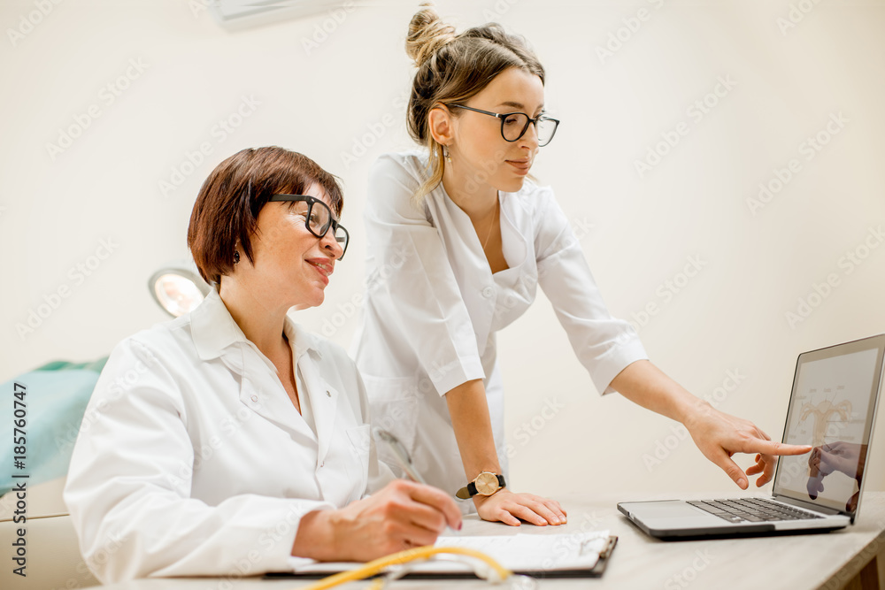 Obraz premium Senior doctor and young woman assistant working together with laptop and documents in the gynecological office