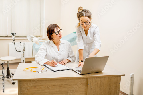 Senior doctor and young woman assistant working together with laptop and documents in the gynecological office