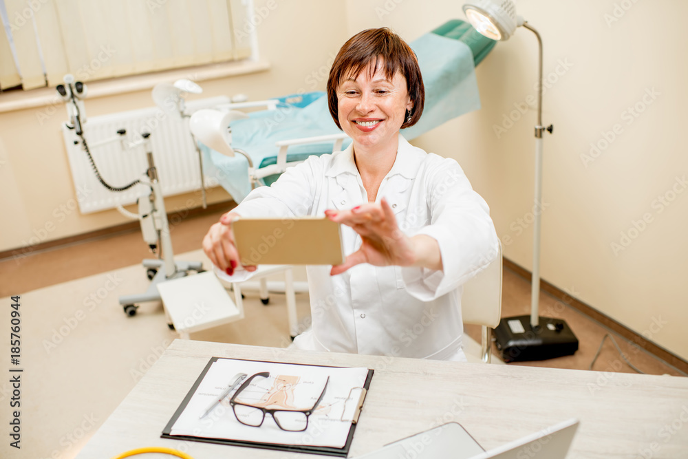 Smiling seinor doctor making selfie photo sitting in the gynecological office