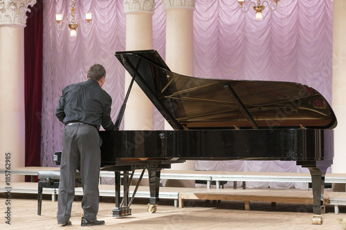 Bild auf Leinwand A man in black tunes a black grand piano