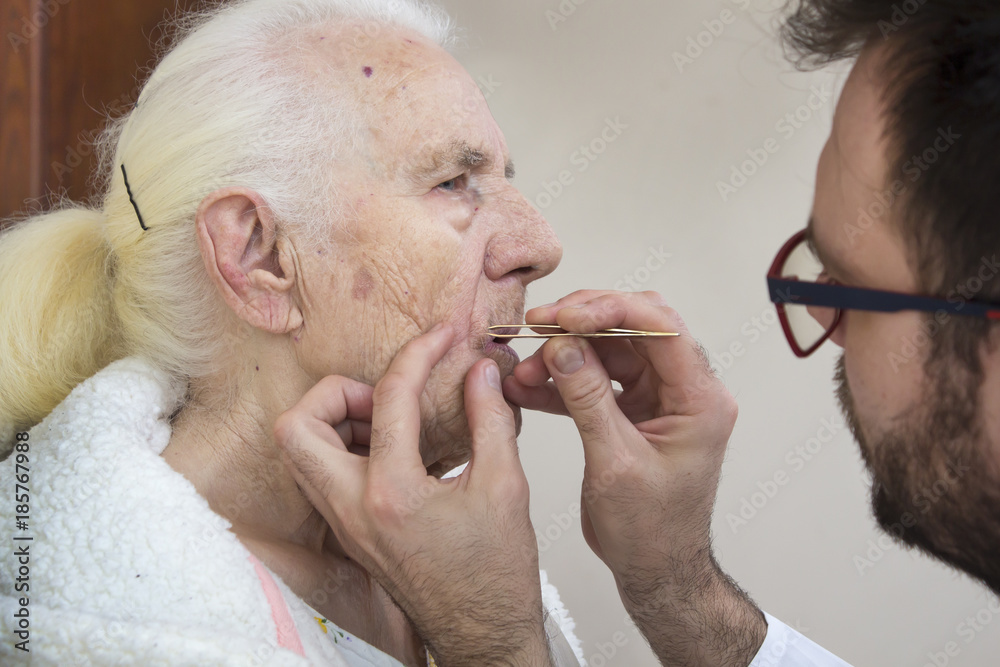 Zabiegi pielęgnacyjne na twarzy starej kobiety. Usuwanie włosów z twarzy pęsetą.  - obrazy, fototapety, plakaty 