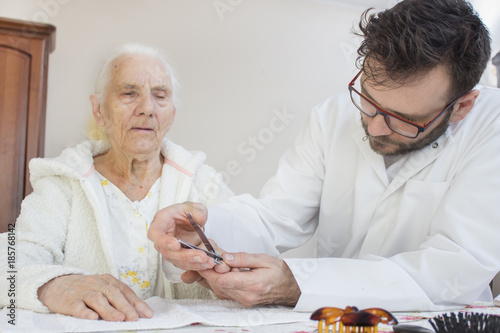 Pielęgniarz w białym kitlu obcina paznokcie u rąk bardzo starej kobiecie.