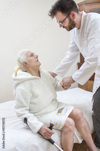 Pielęgniarz pomaga podnieść się z lóżka starej kobiecie.