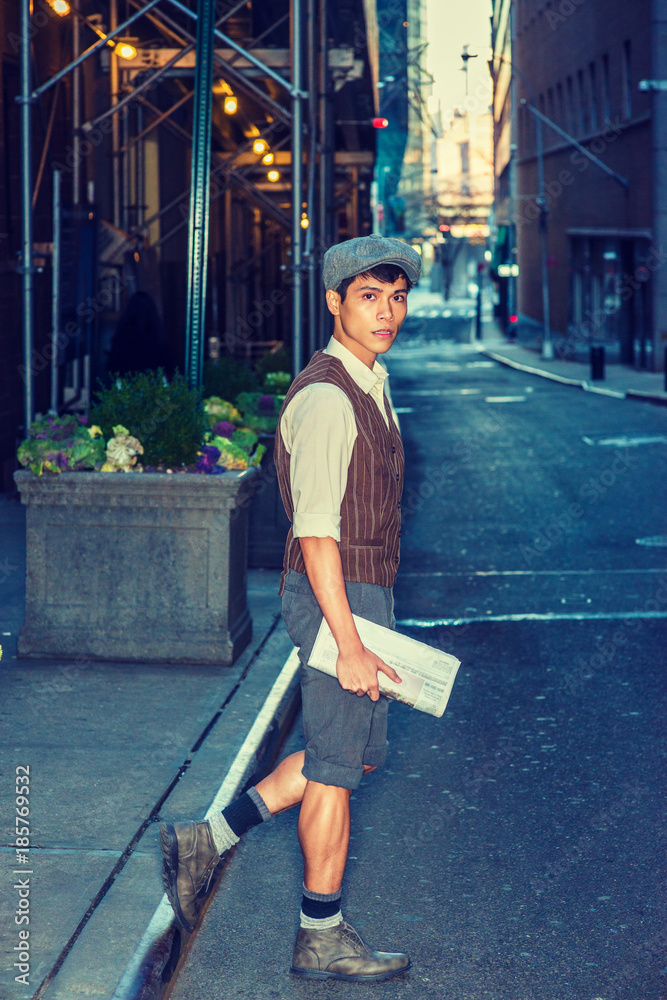 City Wearing cap, shirt, patterned gray pants, boot shoes, holding newspaper, American college student walking, crossing narrow street in New York. Filtered effect... Stock-foto | Adobe Stock