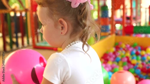 Sweet modest little girl playing in game center. Portrait of little girl playing on the Playground with a ball pit and a slide. photo