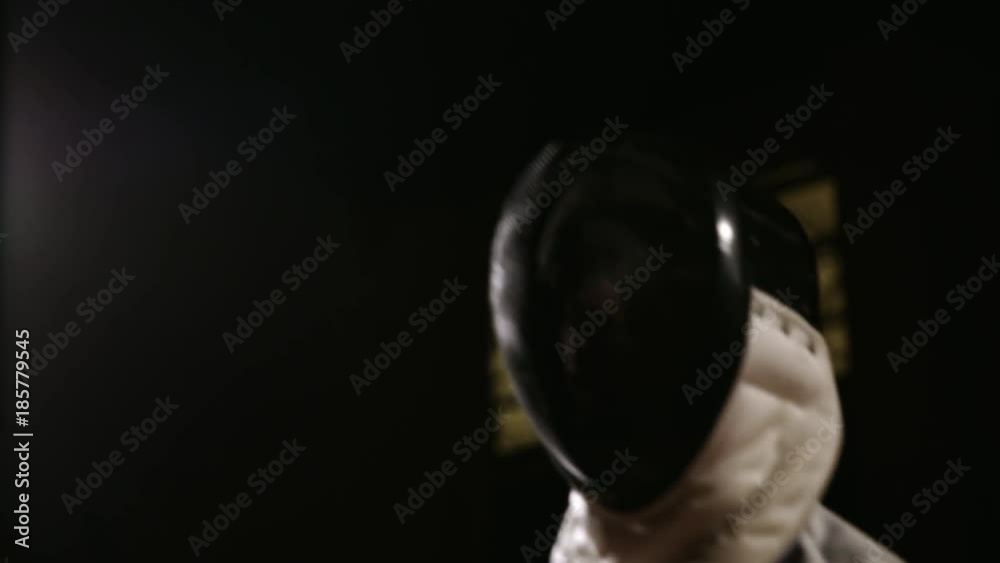 Closeup of a man wears a helmet for fencing grapple with an opponent on a dark background with. Closeup of a man wears a helmet for fencing grapple with an opponent on a dark background with.