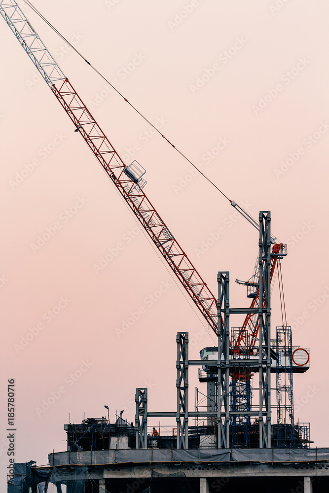 cranes on top of under construction high-rise building at twilight