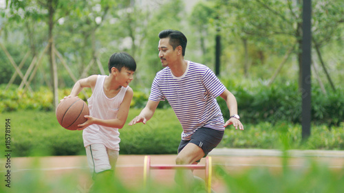 Asian father & son playing basketball in garden in morning