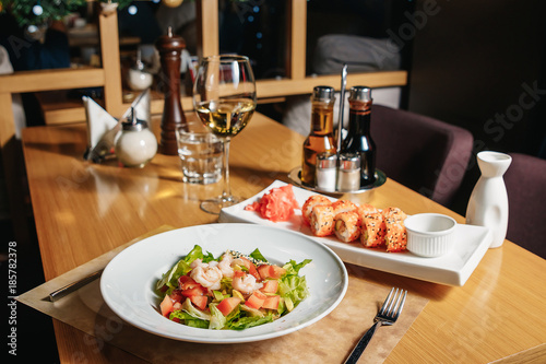 Salad of shrimp, avocado, tomato, lettuce and lemon. A white plate, a table in the restaurant. Sushi Sesame Maki.