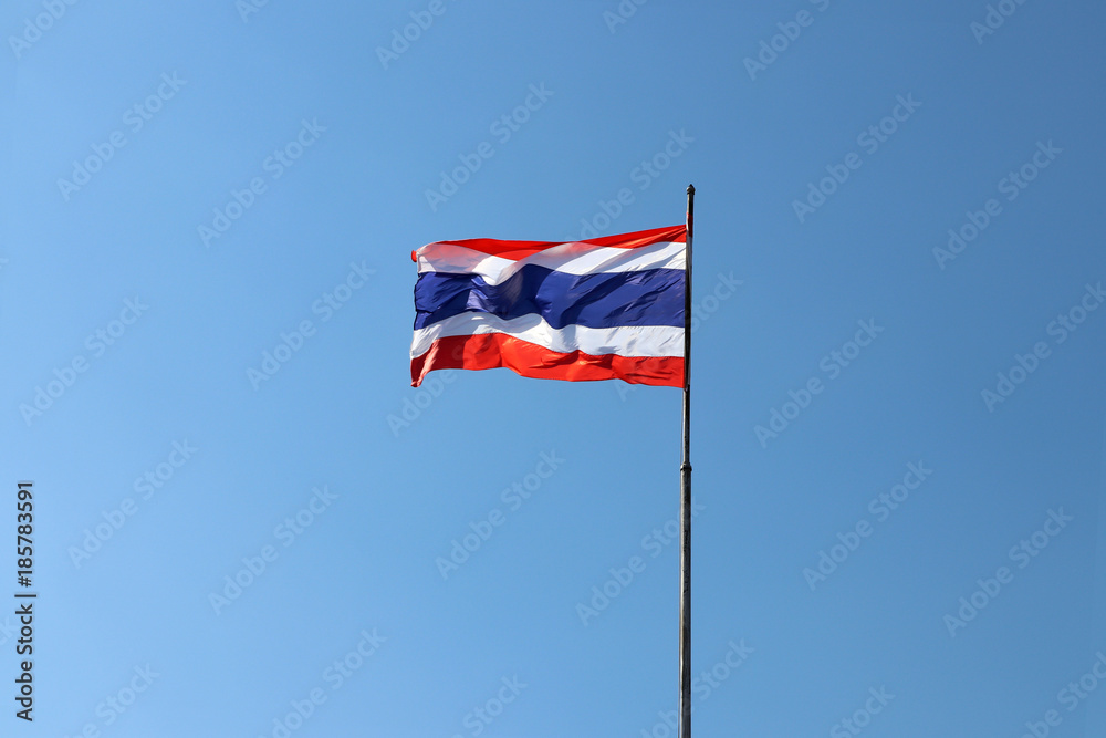 Thai national flag in blue white and red color on the flagstaff blowing with the wind on blue sky background. National flag of Thailand, three color on the fabric.