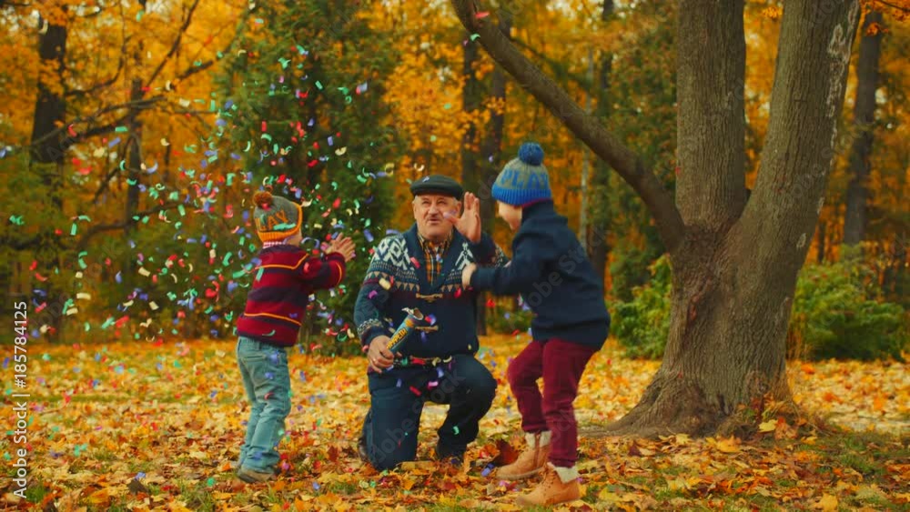 Grandfather is exploding party cracker in the autumn park with his grandsons Grandfather is exploding party cracker in the autumn park with his grandsons