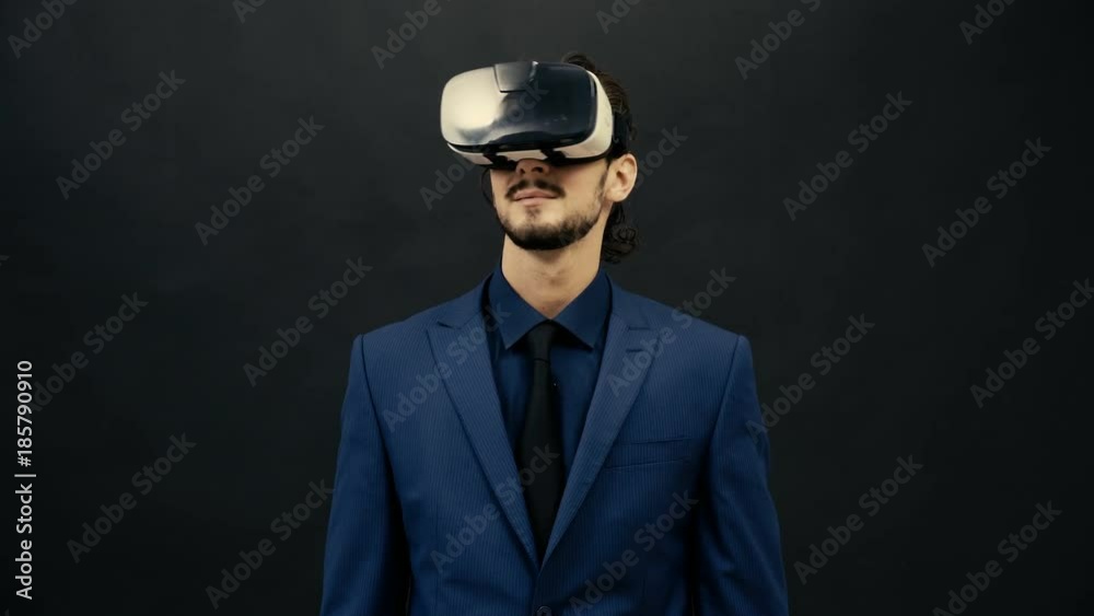 Man in suit wearing VR headset on black studio background experiencing virtual reality. Virtual gestures Man in suit wearing VR headset on black studio background experiencing virtual reality. Virtual gestures