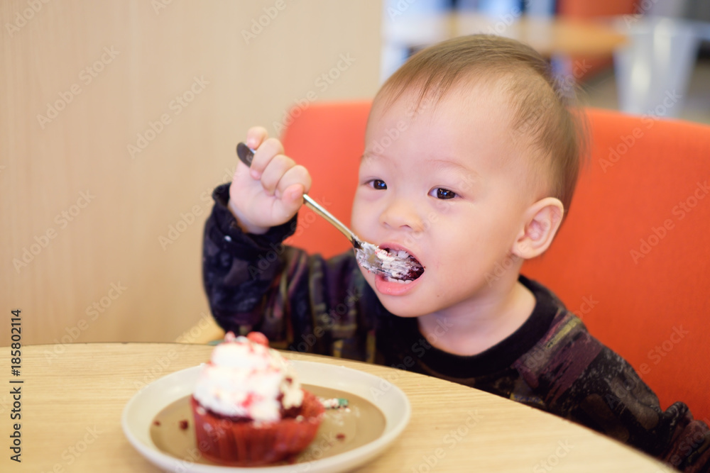 Cute Happy Smiling little Asian 18 months / 1 year old toddler baby boy child eating cupcake with fork, he's sitting on chair at restaurant, Children & Self feeding concept, Soft & Selective focus Cute Happy Smiling little Asian 18 months / 1 year old toddler baby boy child eating cupcake with fork, he's sitting on chair at restaurant, Children & Self feeding concept, Soft & Selective focus