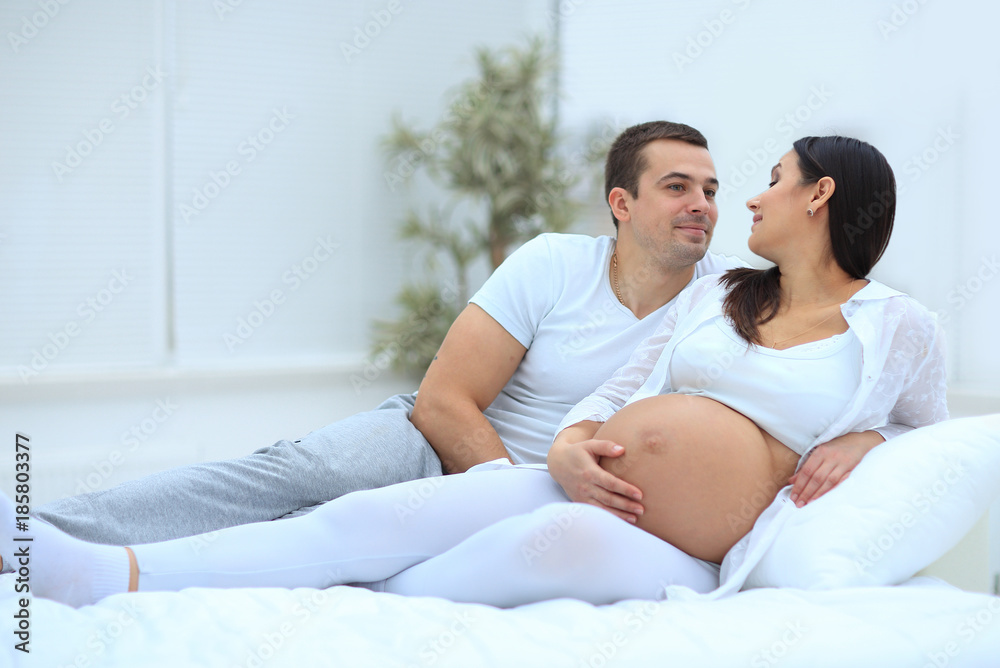 husband and pregnant wife lying on the bed in the bedroom. husband and pregnant wife lying on the bed in the bedroom.