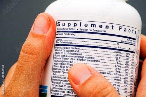 White plastic jar with supplement facts of multivitamins in person hands. photo