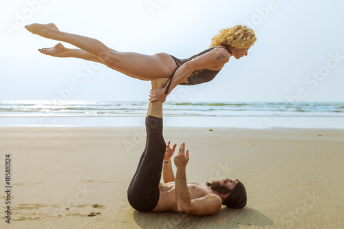 Couple of beautiful people practicing acro yoga on the beach at sunset in Goa, India photo