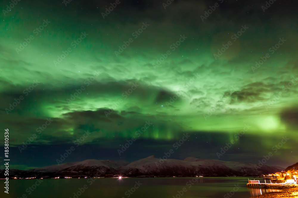 Amazing Aurora Borealis in the clouds in North Norway above the mountains and the sea, Tromso City