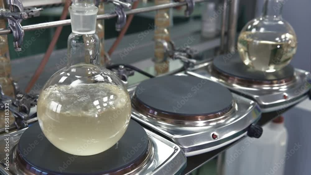 Light liquid is bubbling in a flask under laboratory conditions. Quality control in the laboratory at factory of sparkling wines. Flask is heated with large temperature on the stove in laboratory.