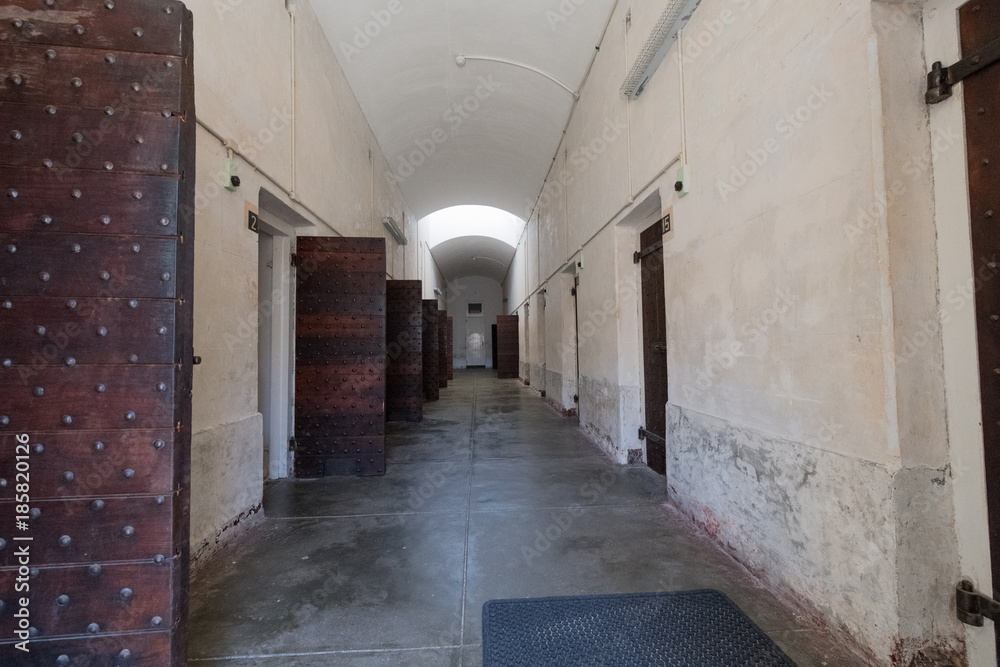Blick in einen Gefängnis-Zellentrakt mit teilweise geöffneten Massivholztüren / Zellen