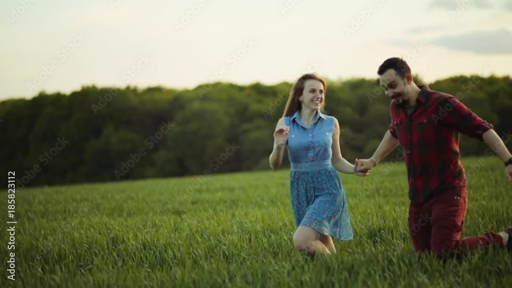 Cute young couple in love holding their hands and happily running through the high grass. True emotions, feeling free. Active lifestyle, leisure time. Romantic atmosphere. Slow motion Cute young couple in love holding their hands and happily running through the high grass. True emotions, feeling free. Active lifestyle, leisure time. Romantic atmosphere. Slow motion