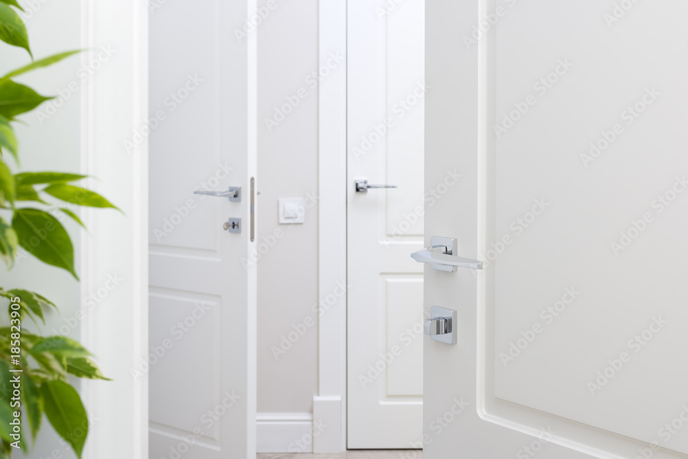 Fototapeta premium Modern chrome door handle on white door. Beautiful interior closeup