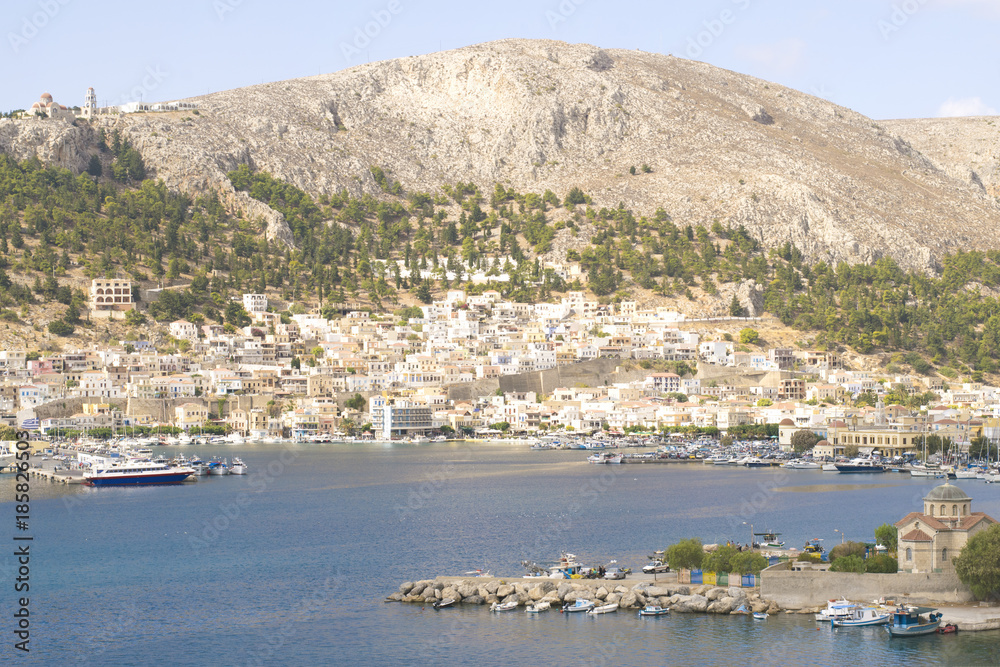 Landscape view on harbor in city Pothia on island Kalymnos. Mountains, monastery, houses and boats in Greece port.