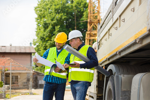 Workers in hardhat and green jacket posing on building site