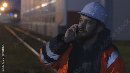 Young and happy worker in hard helmet talking by phone at night. 4k
