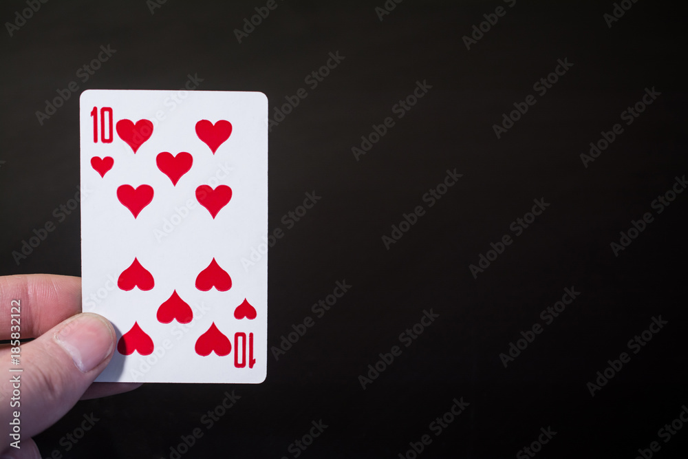 Abstract: man hand holding playing card ten on a black background