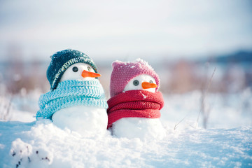 Two little snowmen the girl and the boy in knitted caps and scarfs on snow in the winter. Festive background with a lovely snowman. Christmas card, copy space