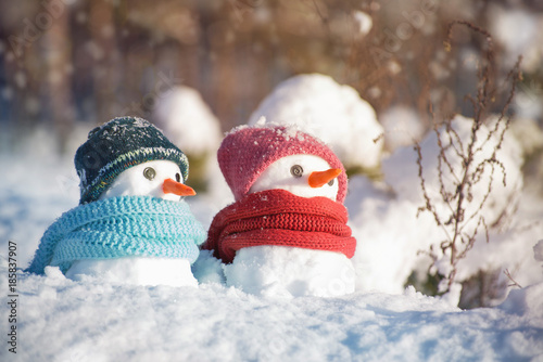 Two little snowmen the girl and the boy in knitted caps and scarfs on snow in the winter. Festive background with a lovely snowman. Christmas card, copy space © isavira