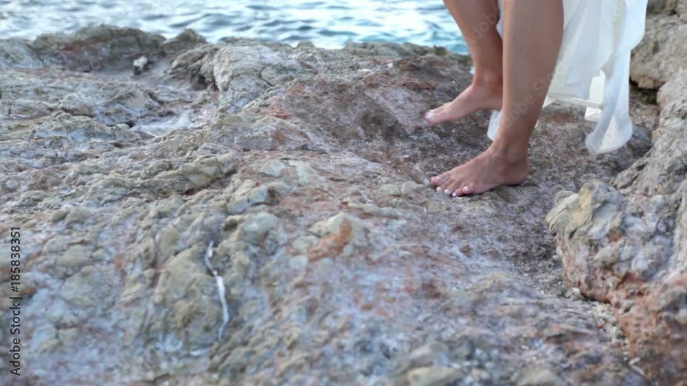 girl is standing on a stone beach by the sea. Body parts. Beautiful female feet with a pedicure on the background of a stone sea shore. Greece