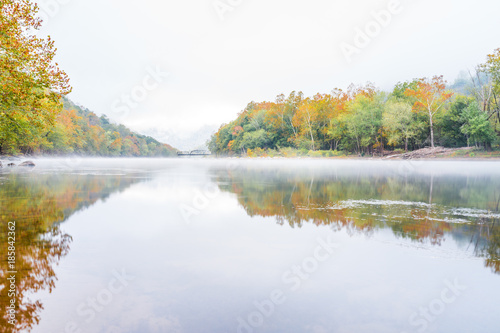 New River Gorge wide canyon water river lake during autumn golden orange foliage in fall by Grandview with peaceful calm tranquil morning bright mist fog