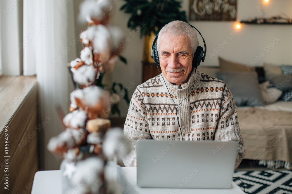 Senior man in headphones using laptop for websurfing. Mature man watching funny sitcom on notebook