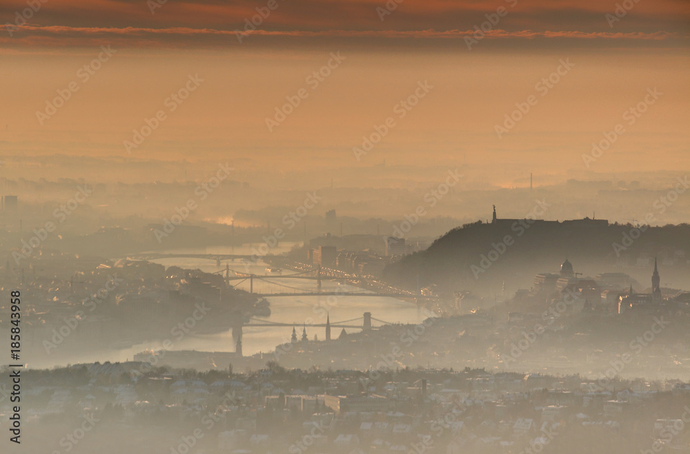 Downtown Budapest capital at sunrise in glowing winter morning mist and clouds with bridges over curving Danube river and Gellert Hill with Liberty Statue and Castle Hill at Buda side, Hungary Europe