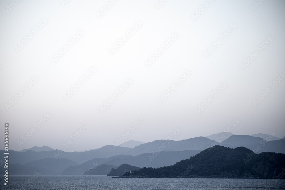 Layers of hill silhouettes, forming different shades of blue and grey, merging with the sea on a shoreline, peaceful and tranquil view