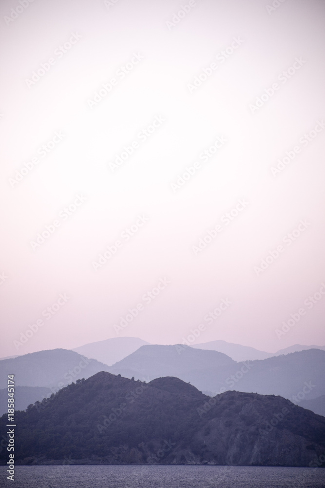 Obraz premium Layers of hill silhouettes, forming different shades of blue and grey, merging with the sea on a shoreline, peaceful and tranquil view