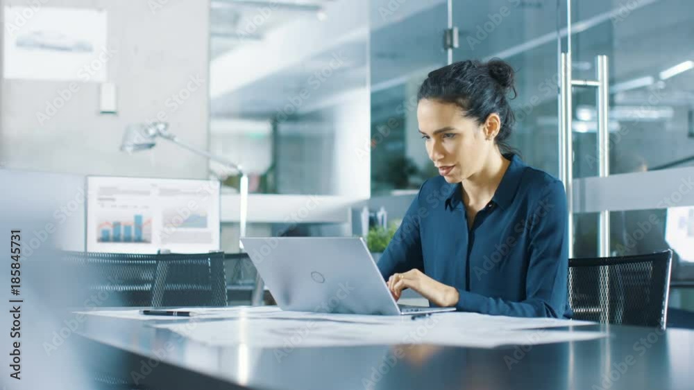 Beautiful Female Data Analyst sitting at the Table Works on a Laptop. Stylish Woman in the Modern Office Environment. Shot on RED EPIC-W 8K Helium Cinema Camera.