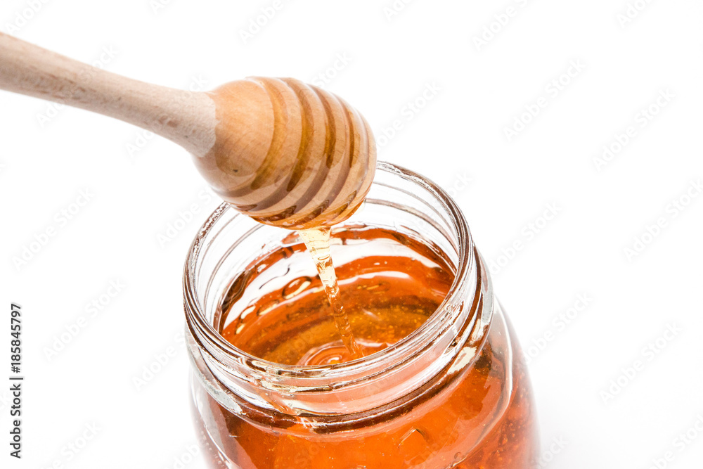 Close up of a honey jar and a honey spoon on a white background from the above Close up of a honey jar and a honey spoon on a white background from the above