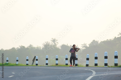 an asian woman is playing violin on the road side in the morning with soften fog