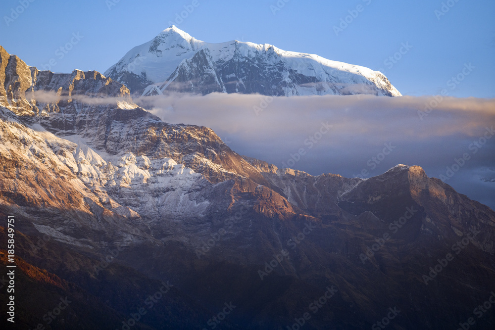 Edge of the Annapurna mountain range rises above the clouds and behind the slope of Fishtail mountain.