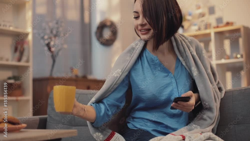Smiling brunette attractive woman smiling drinks tea use pnone sit on the sofa in home christmas tree apartment beauty couch cup focused girl holding reading indoors slow motion Smiling brunette attractive woman smiling drinks tea use pnone sit on the sofa in home christmas tree apartment beauty couch cup focused girl holding reading indoors slow motion