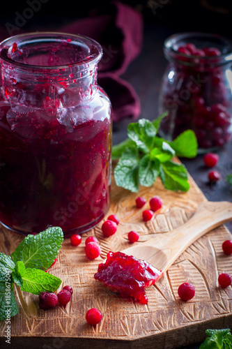 Cowberry jam in a glass jar on a wooden board, selective focus