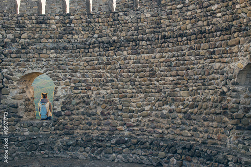 The girl with the backpack vest. Sitting in the window of the fortress, looking at the sunrise tavern. Tourist traveler photo