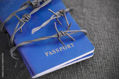 Blue Passport behind barbed wire on a gray textile background, close-up